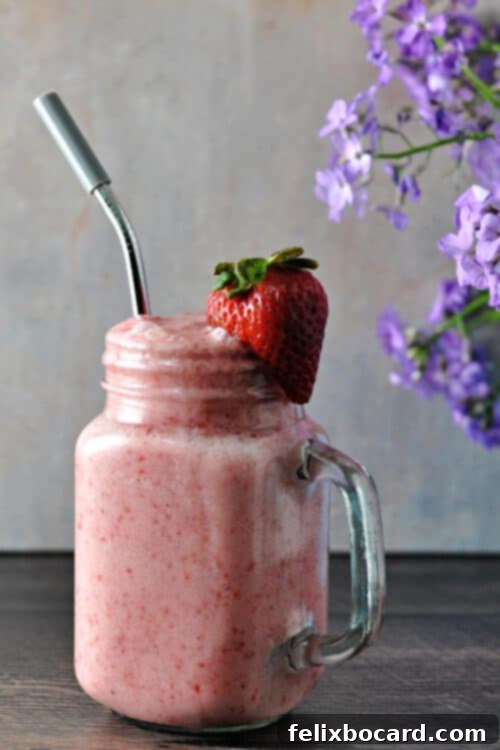 Keto Strawberry smoothie in a mason jar glass garnished with a strawberry with a straw in it.