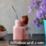 Keto Strawberry Smoothie garnished with a fresh berry. Purple flowers and a bowl of berries in the background