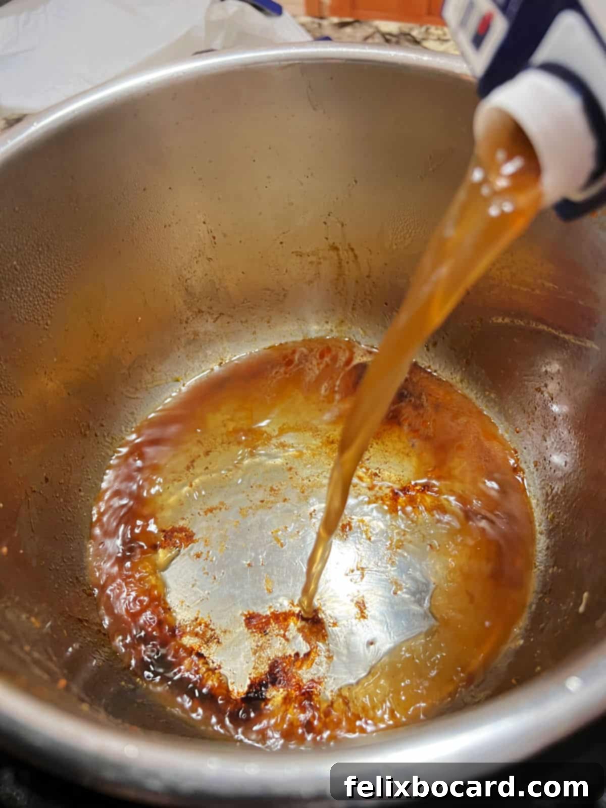 Adding broth to the Instant Pot to deglaze the pot after searing the pork.