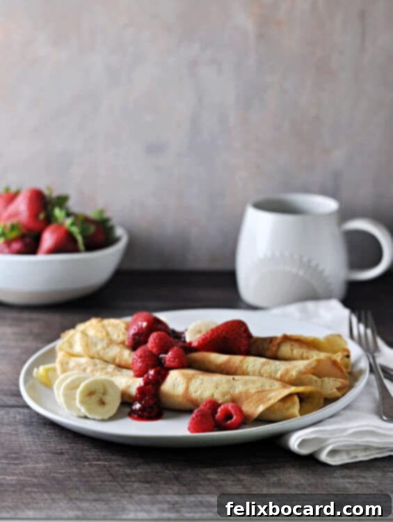 Luscious Dairy Free Almond Milk Crepes 2 Three crepes neatly folded on a plate, adorned with fresh berries and a rich berry sauce, inviting a delightful breakfast experience.