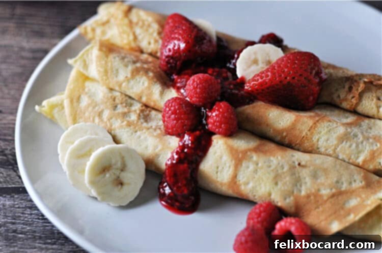 Luscious Dairy Free Almond Milk Crepes 5 A close-up view of freshly made almond milk crepes, elegantly folded and topped with a generous assortment of fresh fruit slices and a rich, vibrant berry sauce, showcasing a delightful and healthy breakfast option.