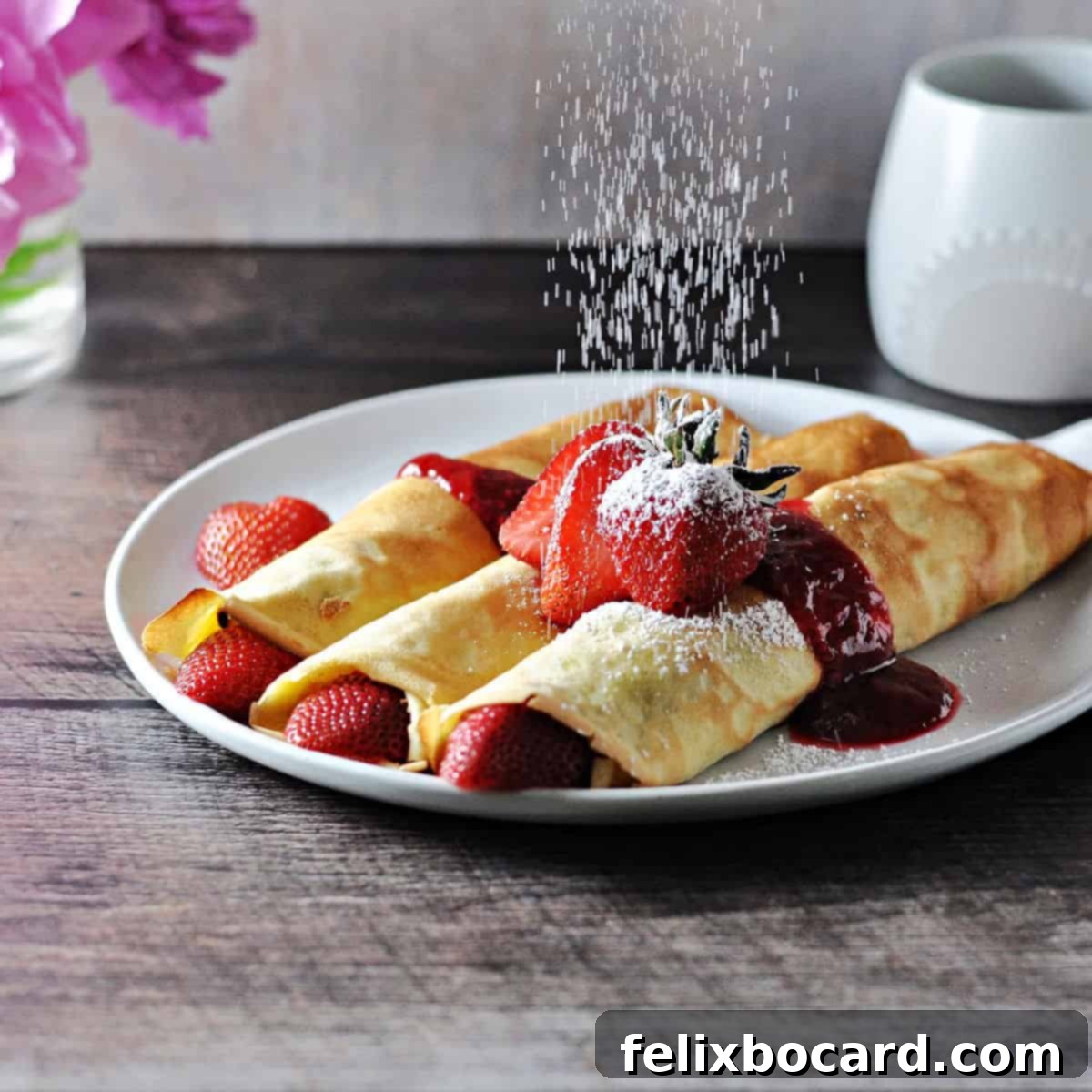 Luscious Dairy Free Almond Milk Crepes 6 Close-up of fluffy almond milk crepes arranged on a plate with fresh fruit, being dusted with a fine layer of powdered sugar, creating a delightful and sweet breakfast presentation.