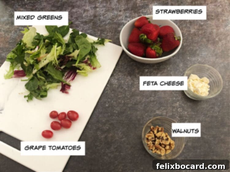 A vibrant display of fresh ingredients for strawberry walnut salad: mixed greens, strawberries, feta cheese, grape tomatoes, and walnuts.