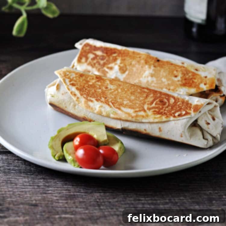 Two grilled stuffed burritos on a white plate garnished with fresh avocado and vibrant tomatoes, ready to be enjoyed.