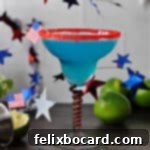 Blue margarita in a red rimmed glass, surrounded by garland stars and some limes