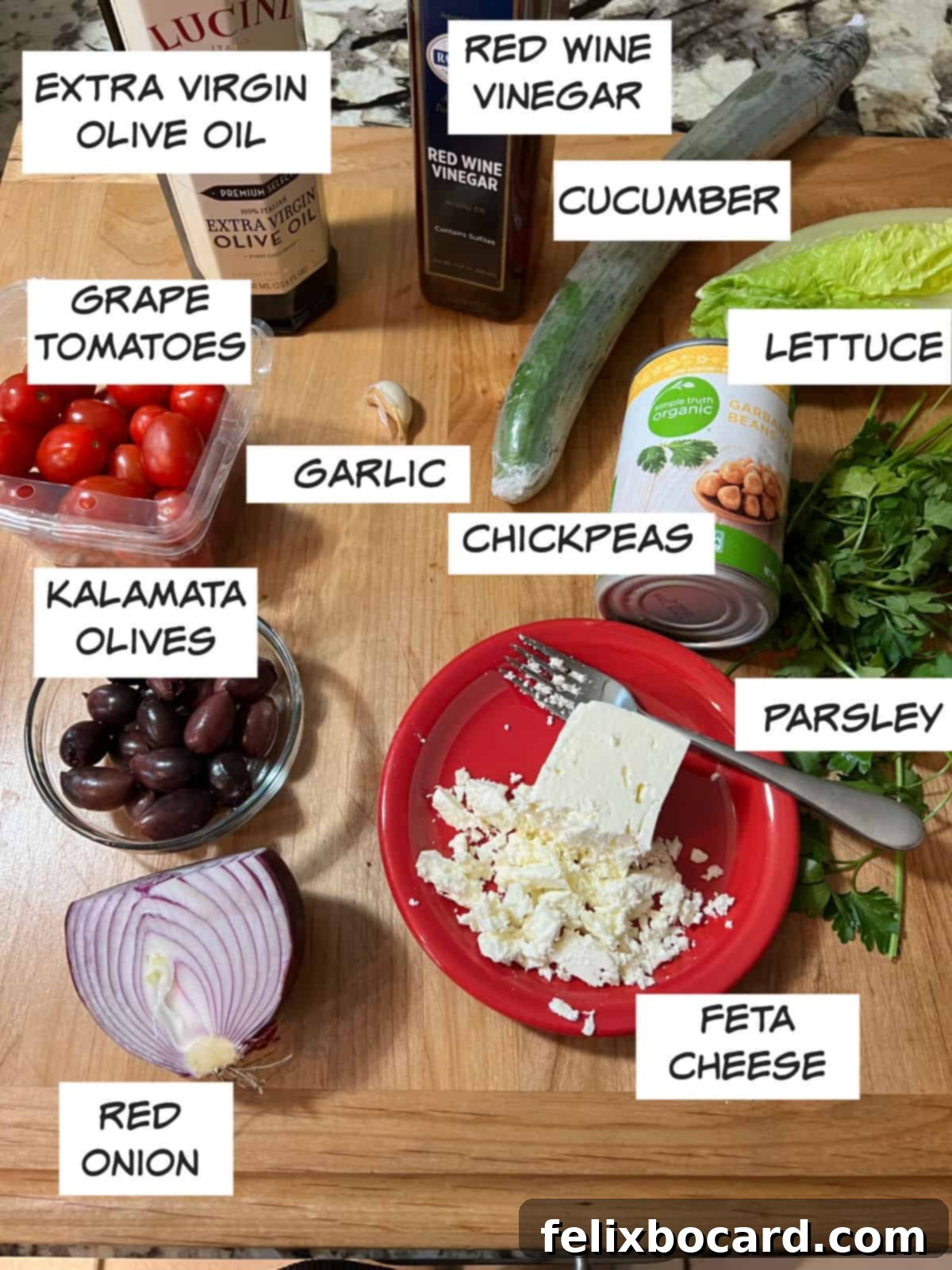 All the fresh ingredients for Mediterranean chopped salad beautifully arranged: grape tomatoes, cucumber, extra virgin olive oil, red wine vinegar, crisp lettuce, wholesome chickpeas, fragrant garlic, fresh parsley, creamy feta cheese, briny Kalamata olives, and vibrant red onion.