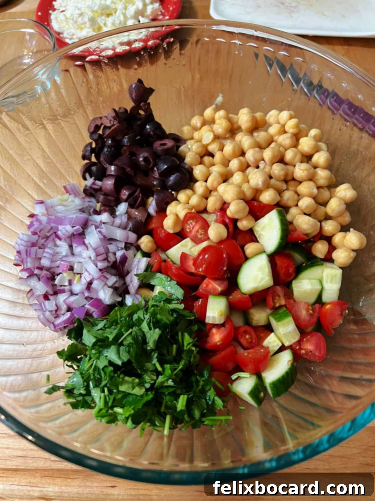 Whisked dressing in a large bowl, with chickpeas, olives, onion, parsley, and drained tomatoes and cucumbers added, ready for marination.