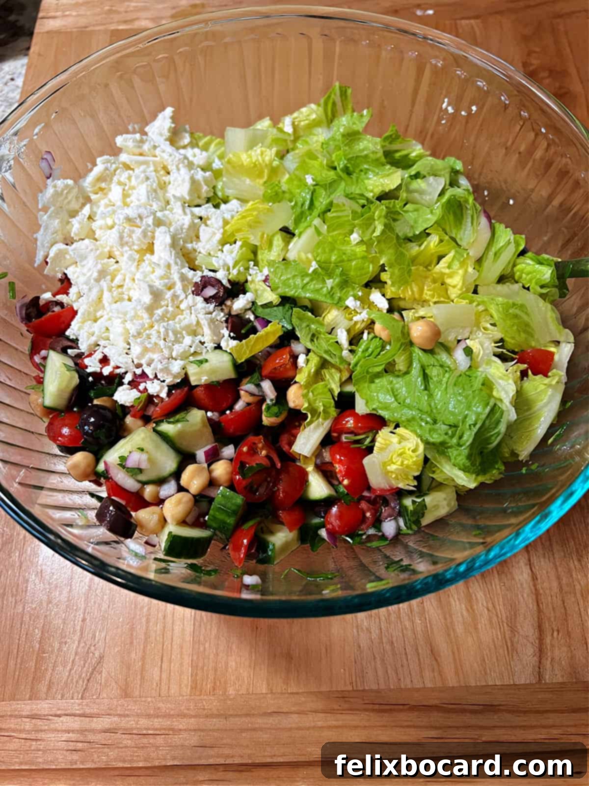 Crisp lettuce and creamy feta cheese are gently added to the bowl, ready for the final toss before serving the Mediterranean chopped salad.