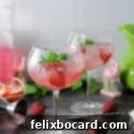 Two pink gin and tonic drinks in wine glasses, garnished with fruit.