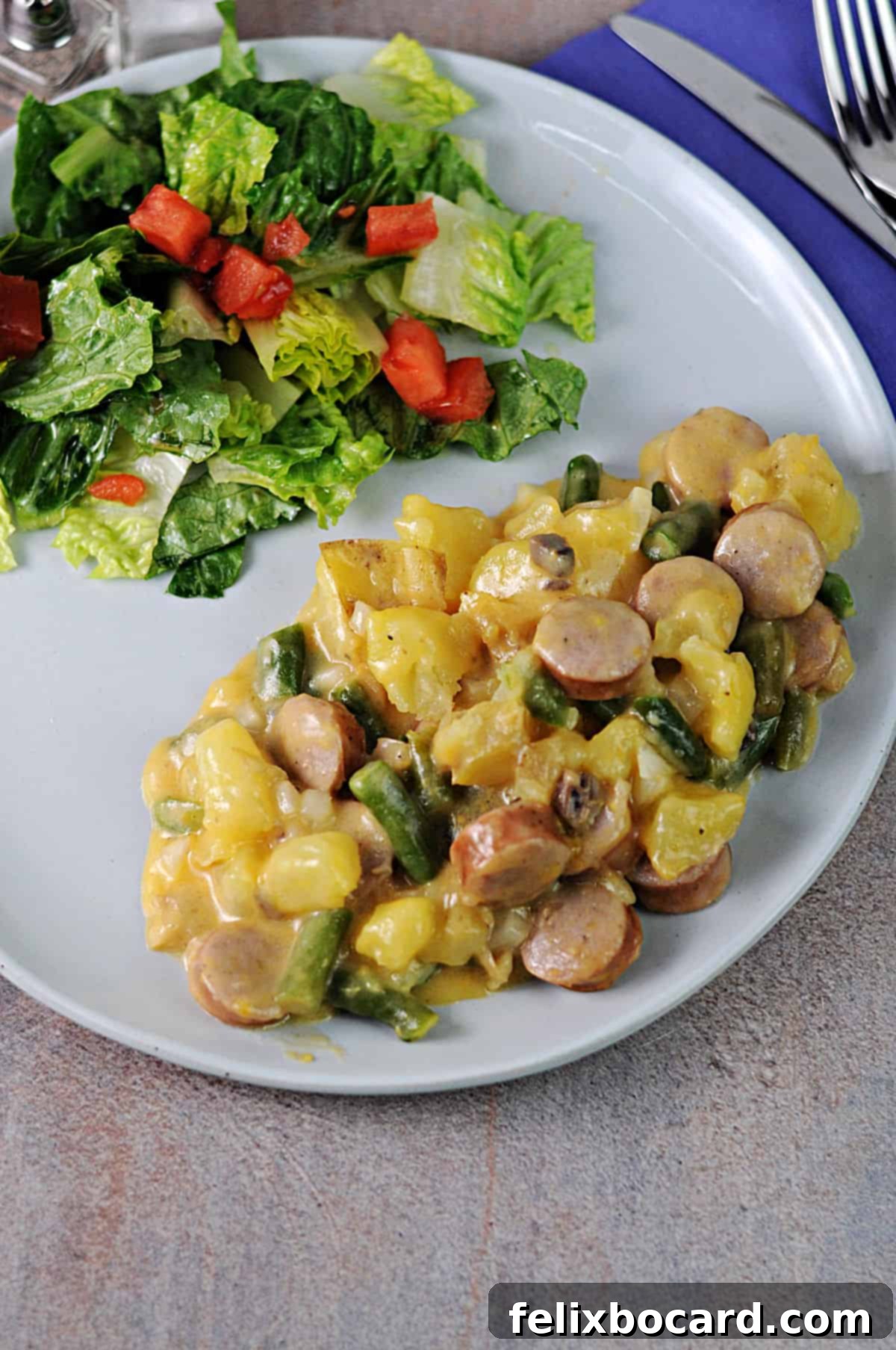 Serving of Cheesy Bratwurst Casserole on a plate with a fresh green salad. The casserole is golden brown and bubbly, showcasing chunks of bratwurst, potatoes, and a creamy cheese sauce.