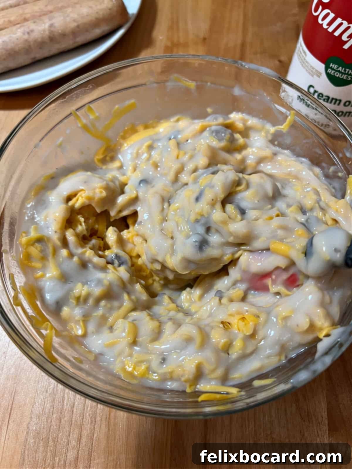 A close-up shot of a bowl where cream of mushroom soup, shredded cheese, and a bit of milk are being stirred together to create the creamy base for the casserole. The texture appears smooth and well-incorporated.