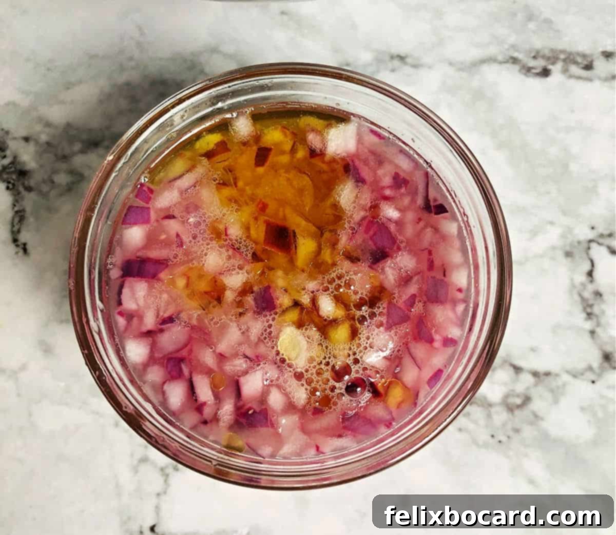 Chopped white onions soaking in a small clear glass cup of cold water, a simple technique to reduce their pungency and mellow their flavor for cooking.