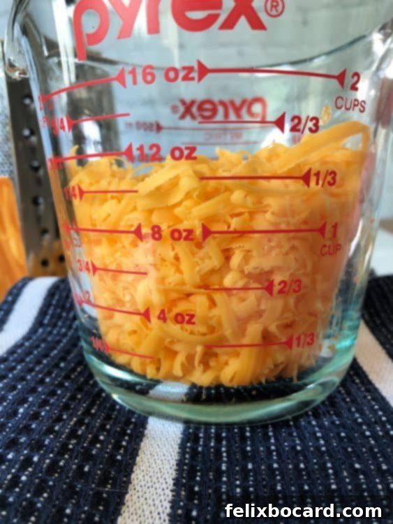 A measuring cup filled with golden shredded cheddar cheese, indicating the generous amount of cheese used in the recipe, promising a truly 'cheesy' experience.