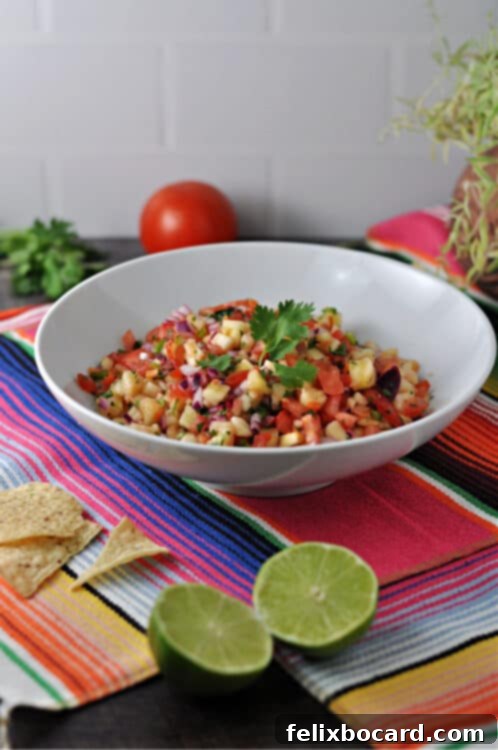 Tropical Heat Salsa 2 A bowl of vibrant Pineapple Habanero Salsa, garnished with fresh cilantro, surrounded by crisp tortilla chips, lime wedges, and ripe tomatoes on a rustic Mexican blanket.