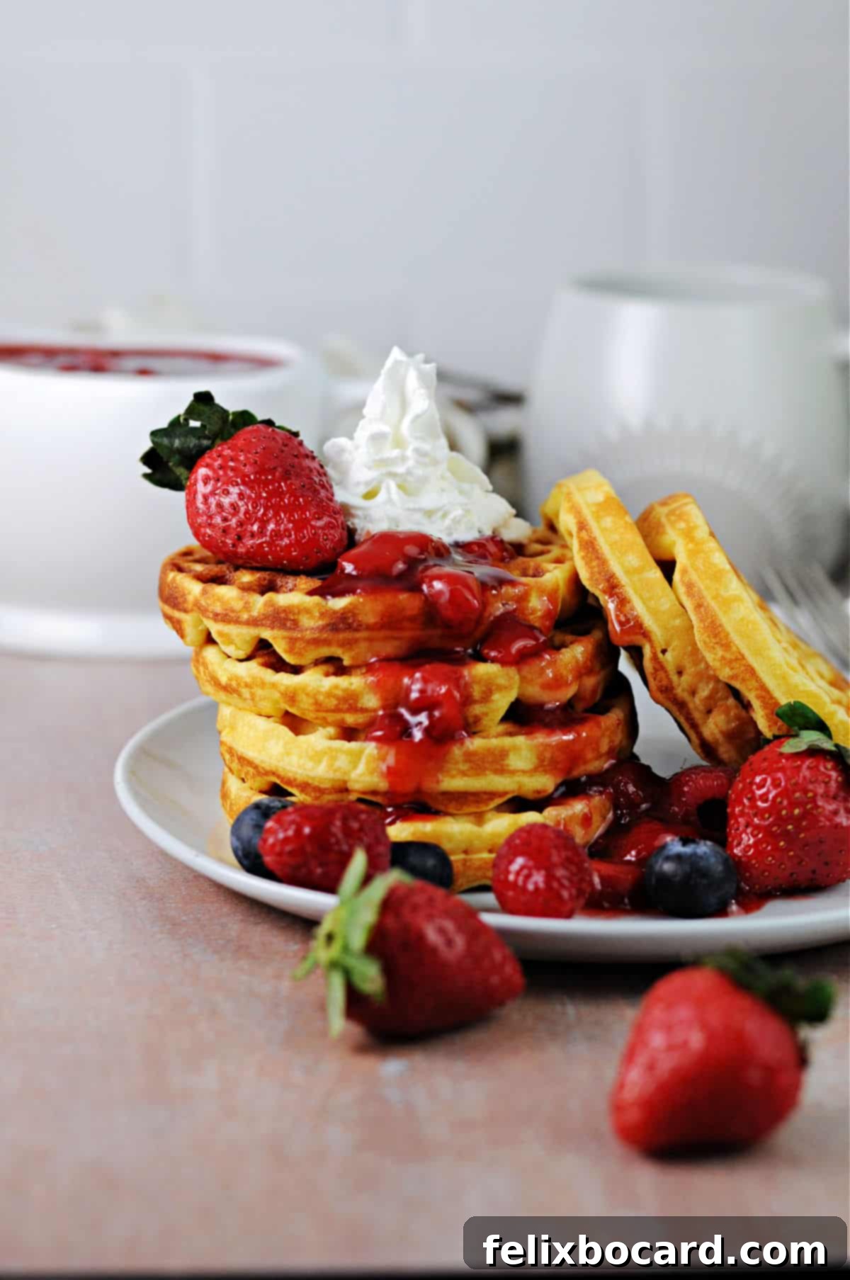 stack of breakfast chaffles (keto waffles) with fruit and a berry sauce, plus whipped cream.