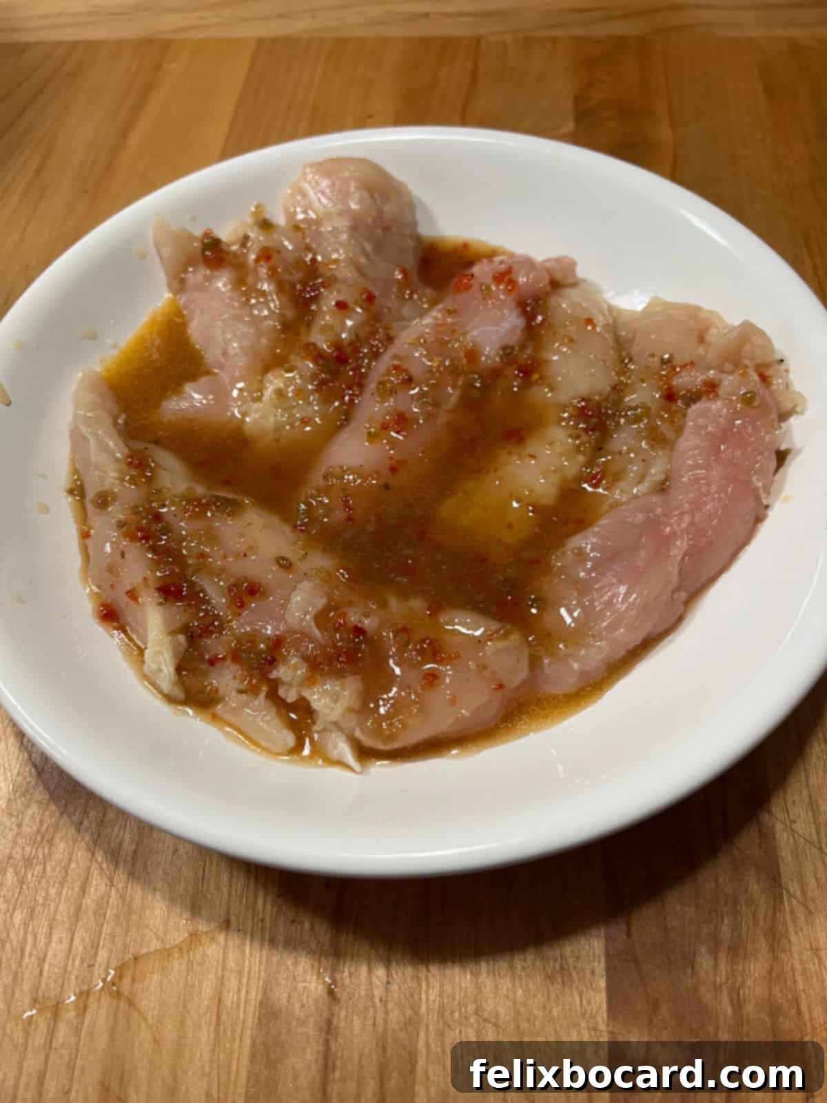Chargrilled Chicken Strips 4 Raw chicken tenders soaking in a zesty Italian salad dressing marinade in a glass bowl, ready for grilling.