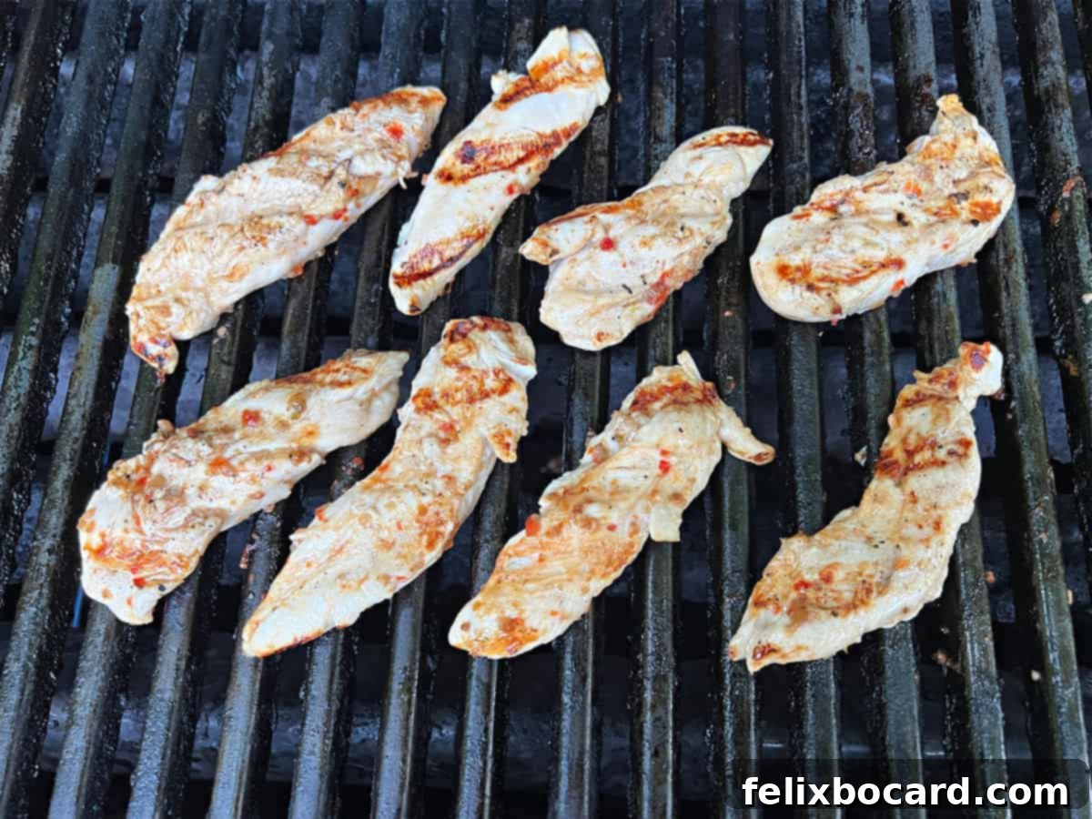 Chargrilled Chicken Strips 5 Chicken tenders sizzling and cooking on hot grill grates, showing developing char marks and a golden-brown hue.