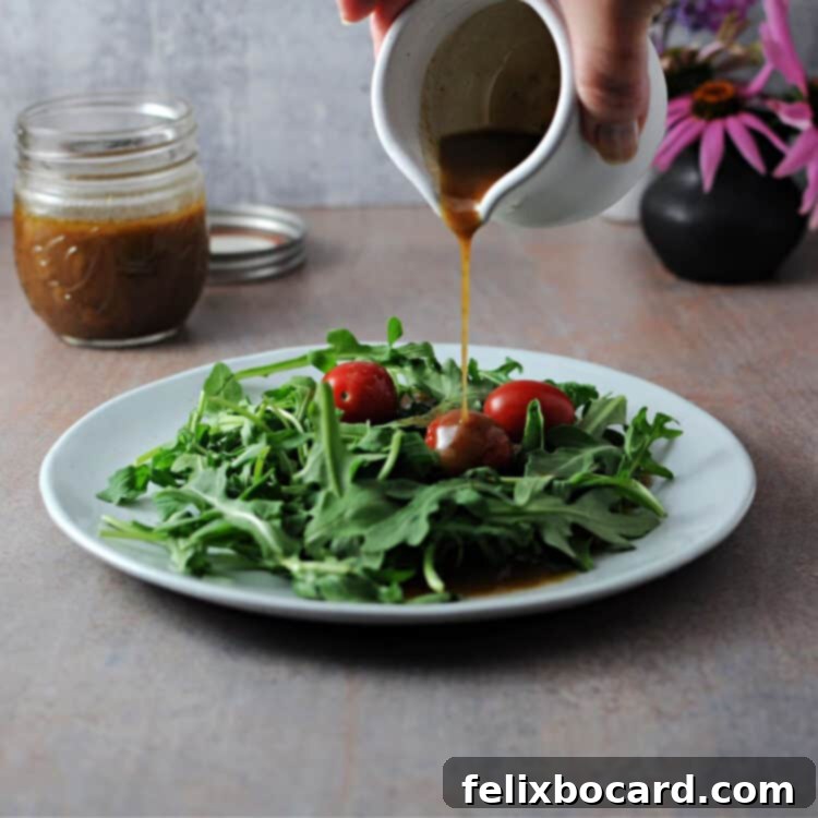 Elevate Your Salad with Homemade Balsamic Vinaigrette 2 A small pitcher pouring homemade balsamic vinaigrette onto a plate of fresh salad greens, showcasing its rich color and inviting texture.