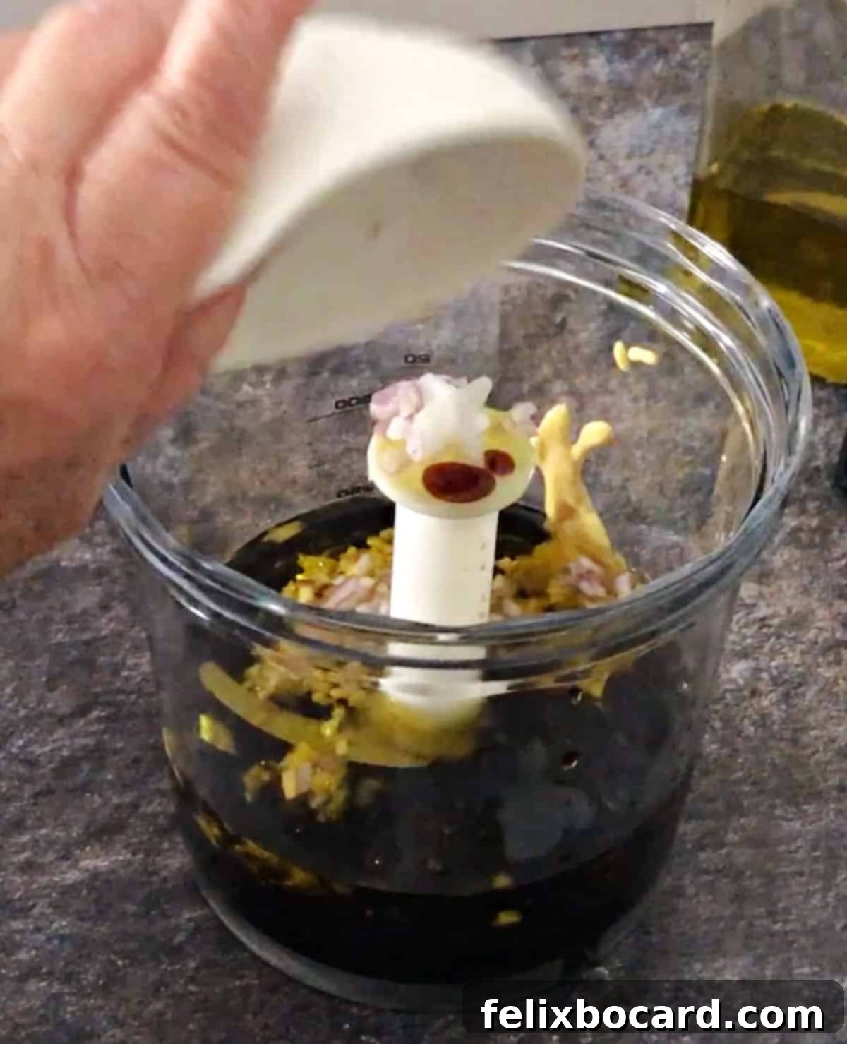 Elevate Your Salad with Homemade Balsamic Vinaigrette 5 Various ingredients for balsamic vinaigrette, including olive oil, balsamic vinegar, honey, and mustard, being added into a small blender cup for mixing.