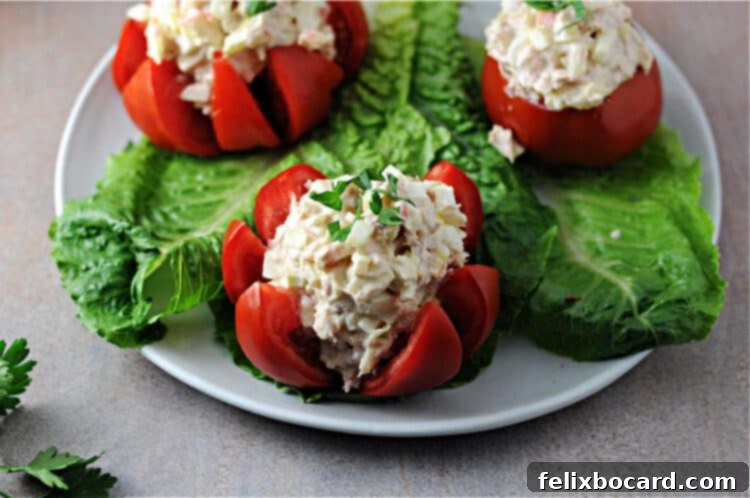 Tuna stuffed tomato on a plate with two others in the background, garnished with fresh herbs.