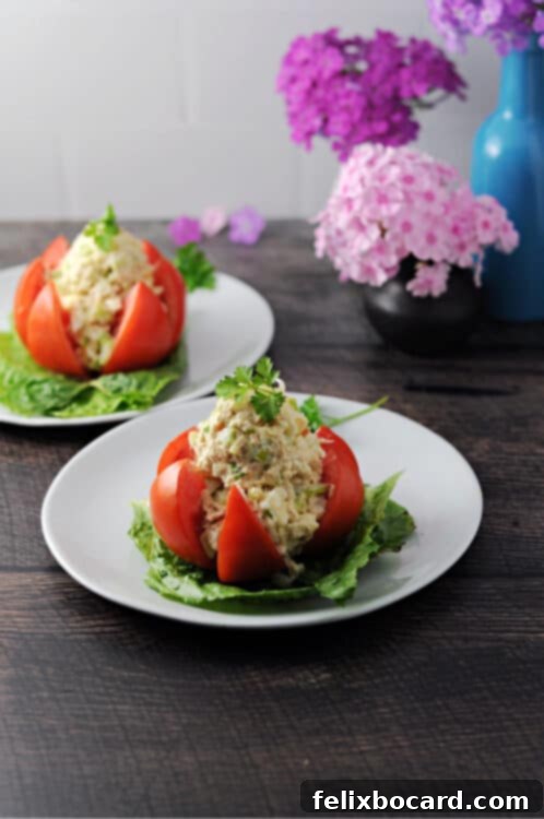 A beautifully presented tuna stuffed tomato on a small plate, with a second serving and floral decoration in the background.