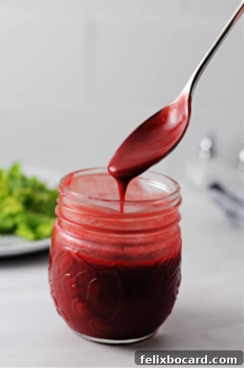 Raspberry balsamic vinaigrette dressing pouring from a spoon into a jar, showcasing its vibrant color and smooth texture