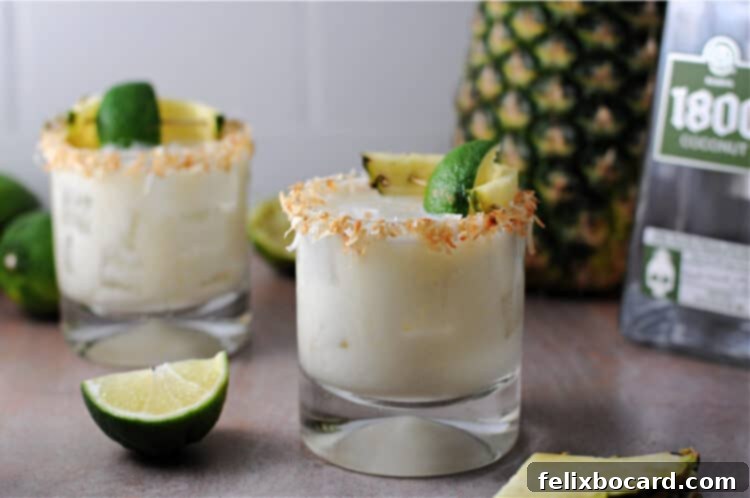 Two vibrant coconut pineapple margaritas garnished with a toasted coconut rim, fresh lime wedges, and a whole fresh pineapple creating a tropical scene.