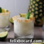 Coconut Pineapple Margarita in a rocks glass garnished with a rim of toasted coconut and a spear of pineapple and lime