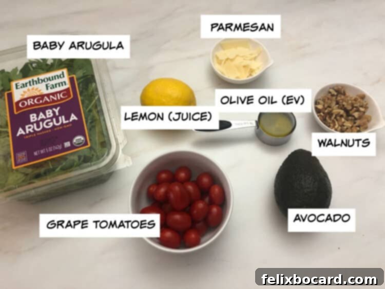 Ingredients for Arugula Avocado Salad including arugula, whole avocado, grape tomatoes, lemon, Parmesan cheese, olive oil, and walnuts.