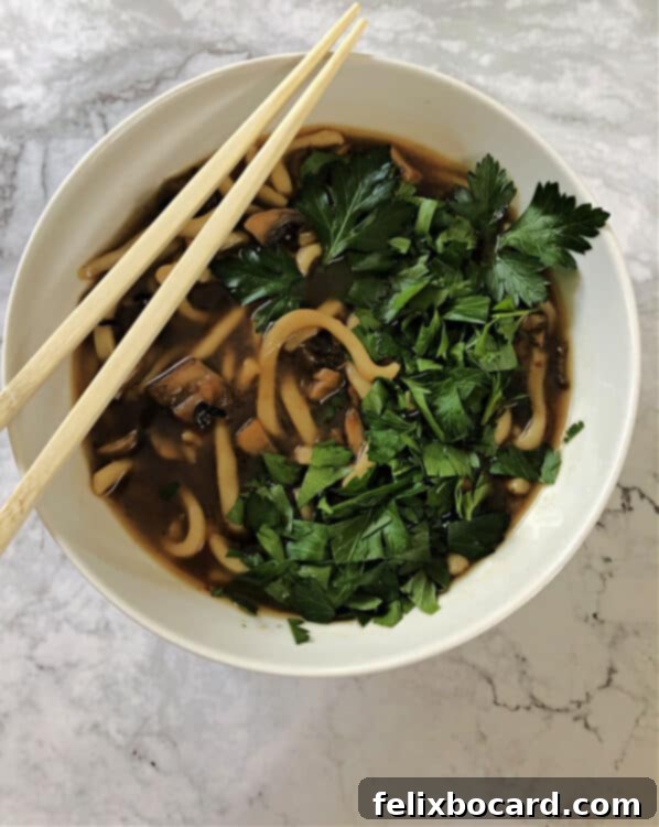 spicy mushroom noodle soup served in a white bowl with chopped frresh herbs on top