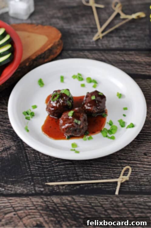 Three perfectly glazed grape jelly BBQ meatballs presented on a pristine white plate, with the rich sauce pooling around them.