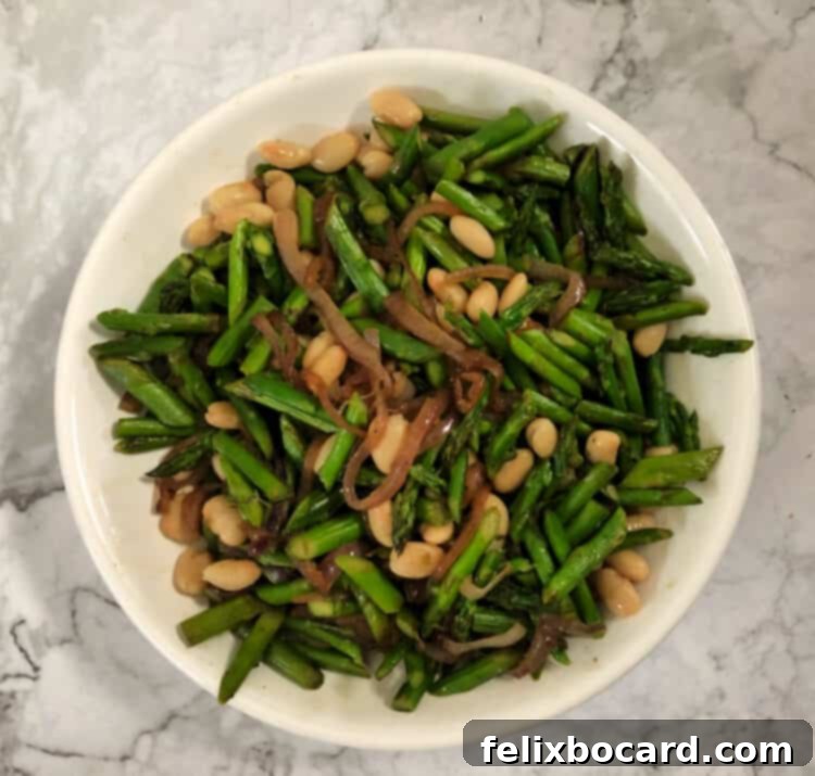 Mixed salad ingredients in a bowl: sautéed asparagus and red onion with cannellini beans