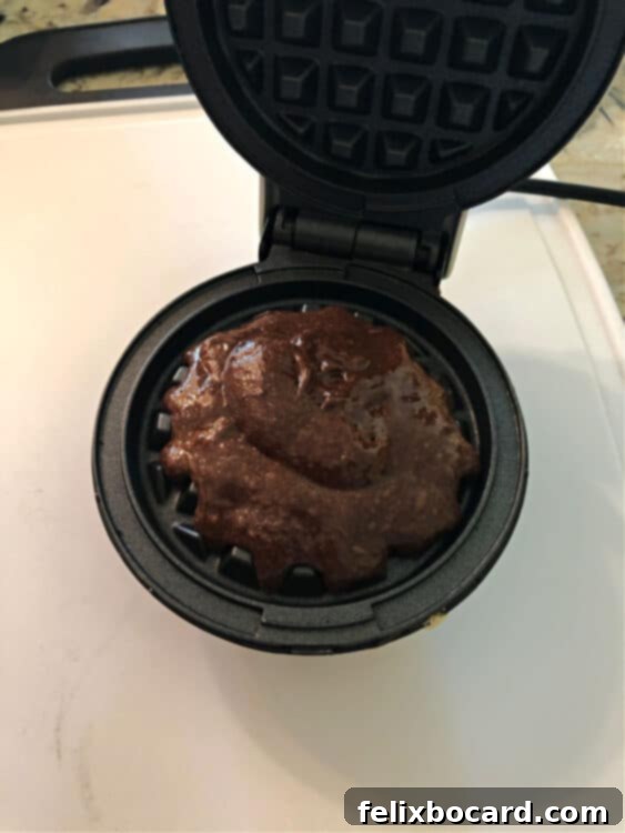 Chocolate cake mix waffle batter being carefully spooned into a preheated Dash mini waffle iron, ready for cooking.