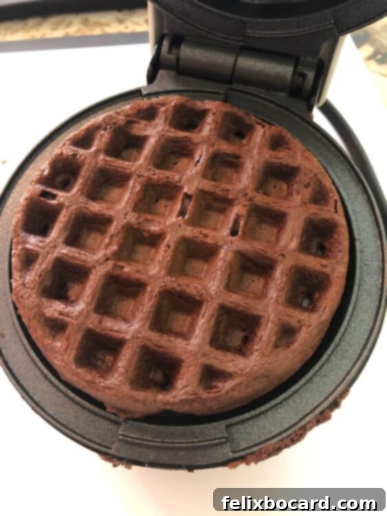 A perfectly cooked, golden-brown chocolate cake mix waffle nestled in a waffle iron, steam gently rising, indicating it's ready to be served.
