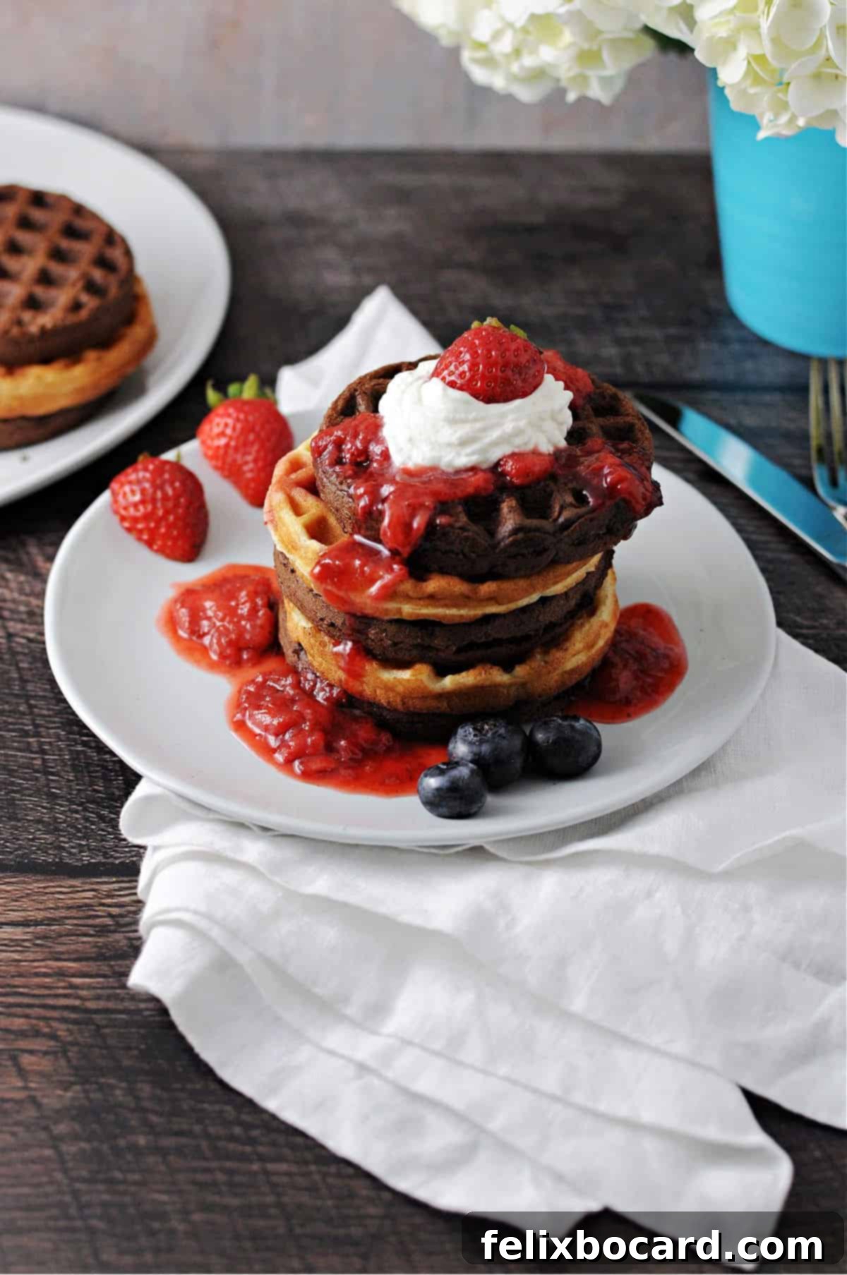 A beautiful stack of golden-brown cake mix waffles, lavishly topped with a vibrant berry sauce and fluffy whipped cream, presented on a rustic wooden board.