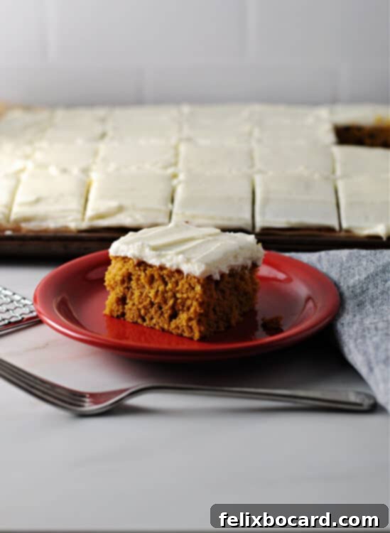 A single pumpkin bar on a vibrant red plate, with an entire pan of freshly baked bars blurred in the background, showcasing the inviting texture and cream cheese frosting.