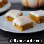 Three pumpkin bars with cream cheese frosting on a white plate, ready to be served.