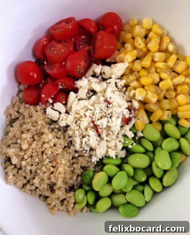 ingredients in a bowl: quinoa, tomato, corn, edamame, and feta cheese