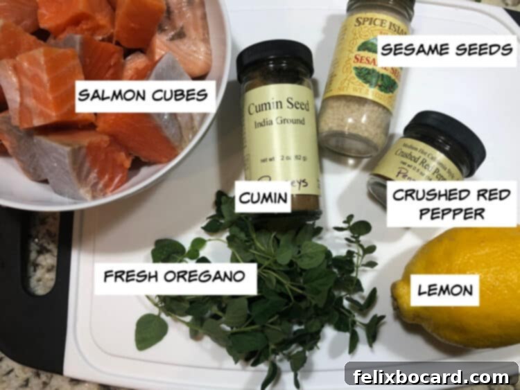 A close-up of the essential ingredients for salmon kabobs: perfectly cut salmon cubes, bright lemon slices, fragrant fresh oregano, sesame seeds, crushed red pepper flakes, and ground cumin.