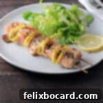 A beautifully presented salmon kabob served on a plate with a fresh green salad, highlighting the golden-brown salmon pieces and charred lemon.