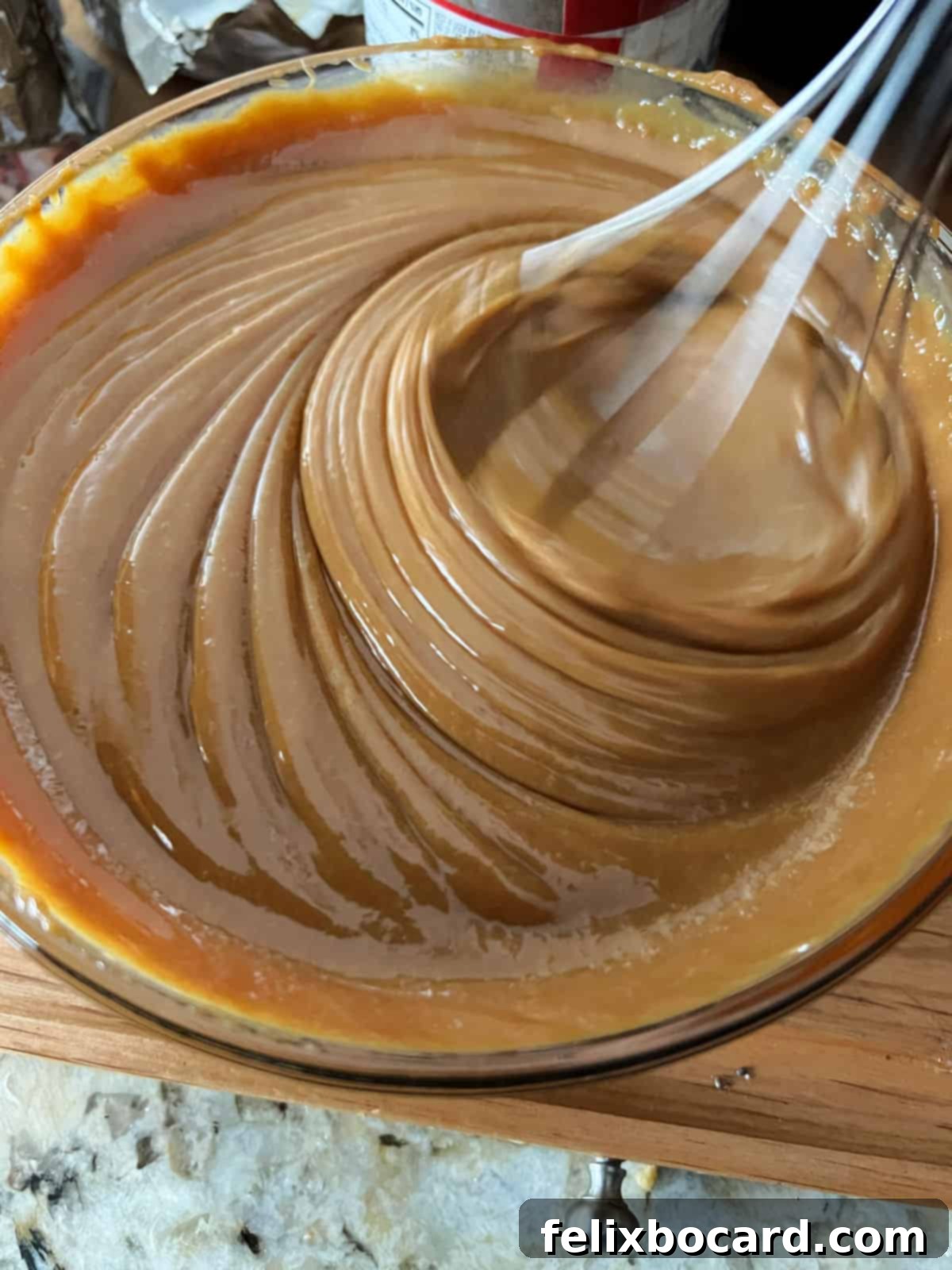 Instant Pot Dulce de Leche 6 Caramel sauce being stirred with a whisk in a bowl, demonstrating the smoothing process.