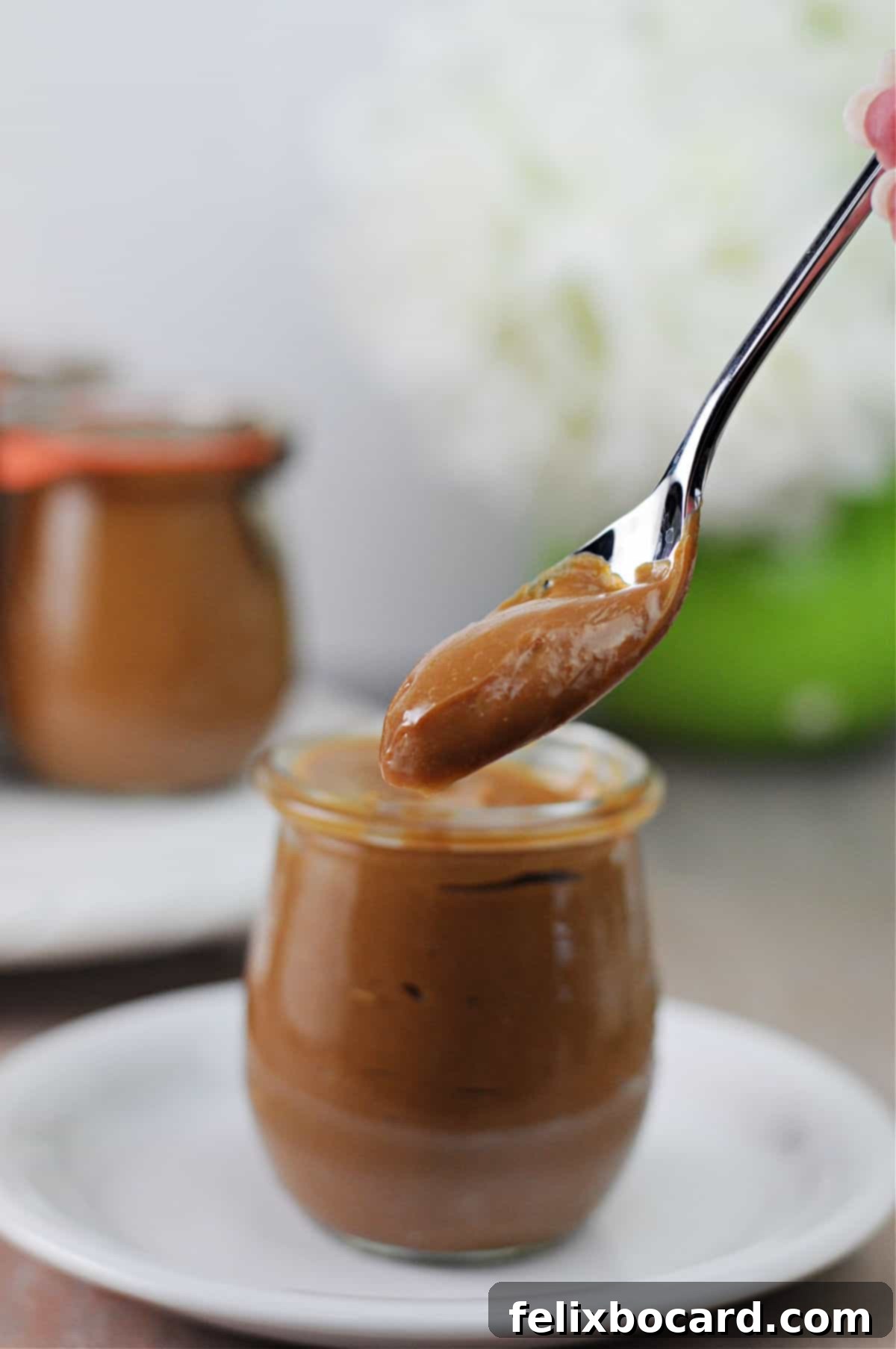 Instant Pot Dulce de Leche 7 A jar of homemade Instant Pot caramel sauce with a spoon dripping sauce into it, showcasing its delicious texture.