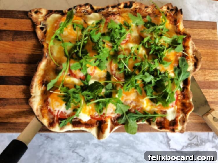 Vegetarian grilled pizza beautifully topped with fresh arugula, added immediately after grilling to gently wilt the greens.