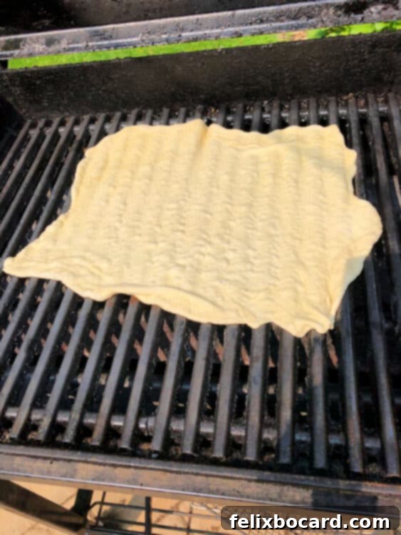 Raw pizza crust placed directly on hot BBQ grill grates, showing the initial stages of cooking with slight bubbling.