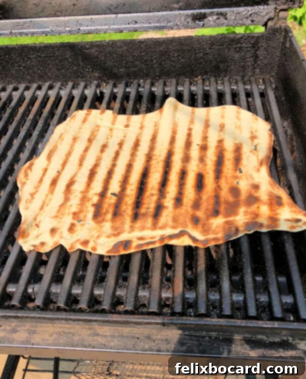 Partially cooked pizza crust flipped on the grill, showcasing the side with distinct grill marks and a firm texture.