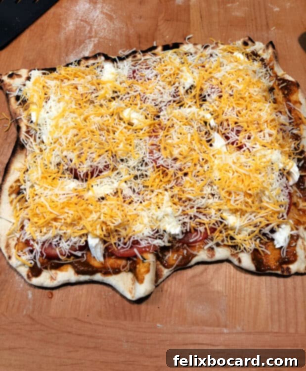 Vegetarian grilled pizza crust on cutting board with a colorful array of toppings including sliced tomato, fresh mozzarella, and shredded cheese.
