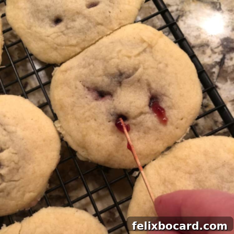 A toothpick being used to carefully add a small drip of raspberry jam to a baked cookie's bite mark.