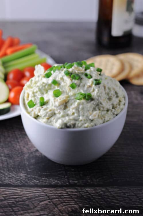 Bold Artichoke Jalapeno Dip 4 A serving of creamy jalapeno artichoke dip in a white bowl, accompanied by an assortment of fresh vegetables and crackers, ready for dipping, highlighting its versatility.
