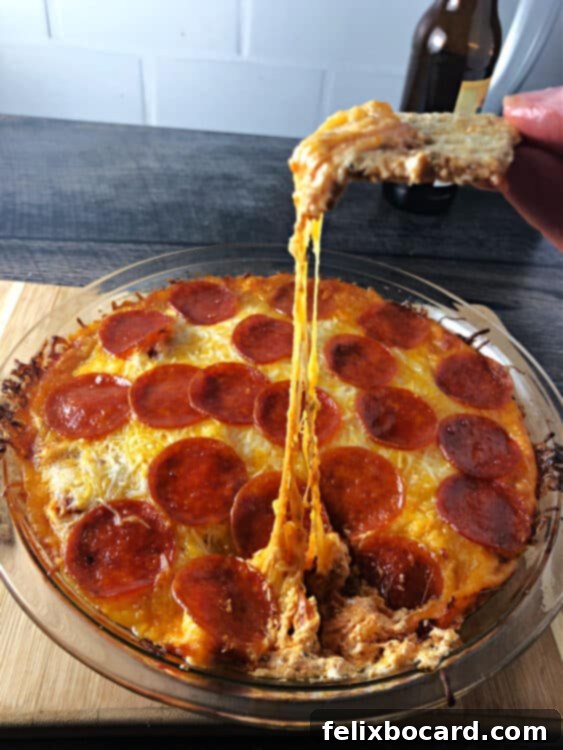 pepperoni dip showing a long pull of melted cheese between the dish and the cracker