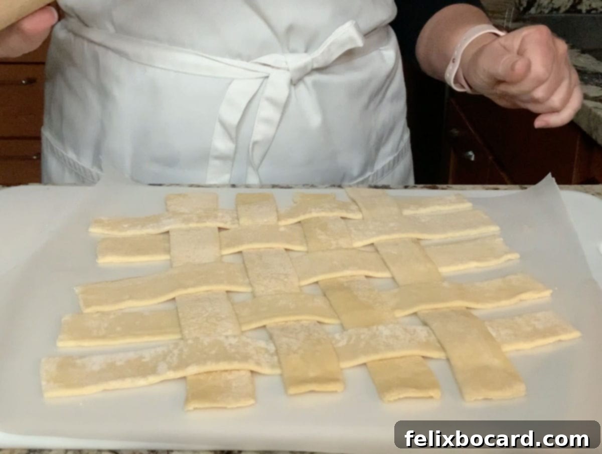 Strips of puff pastry dough woven to make a loose lattice pattern on wax paper.